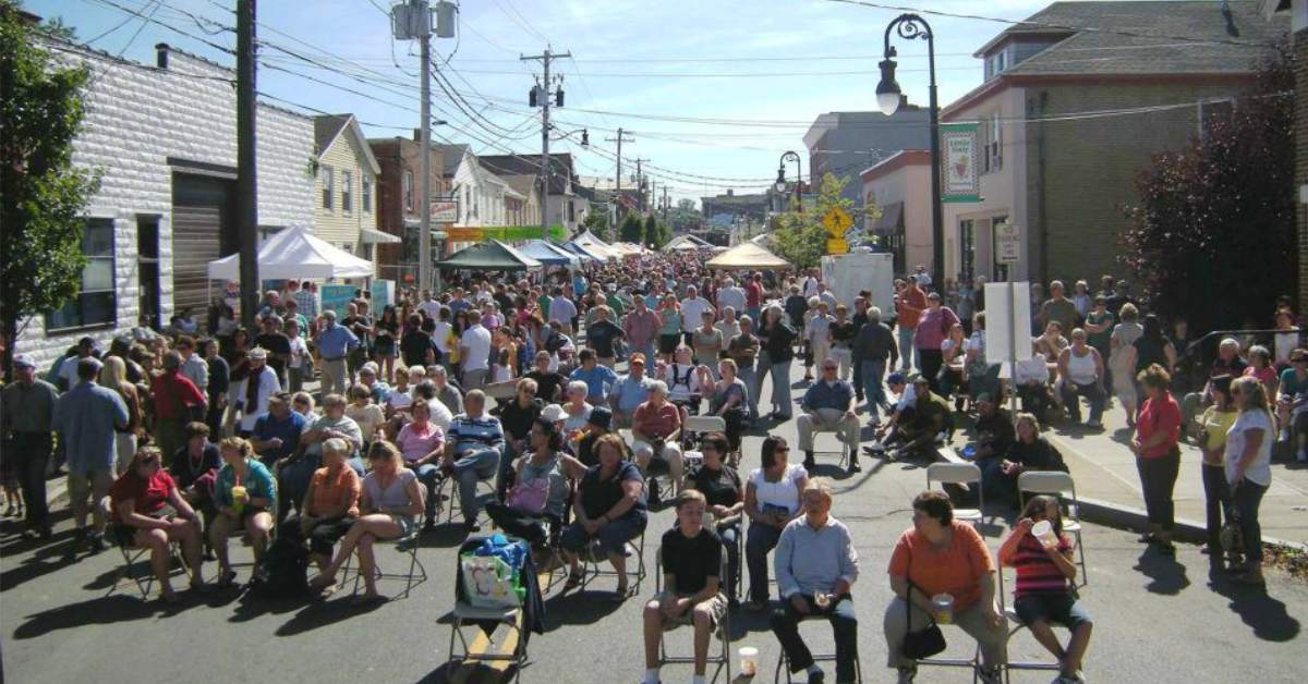 group of people seated in chairs waiting for music outdoors at a street festival