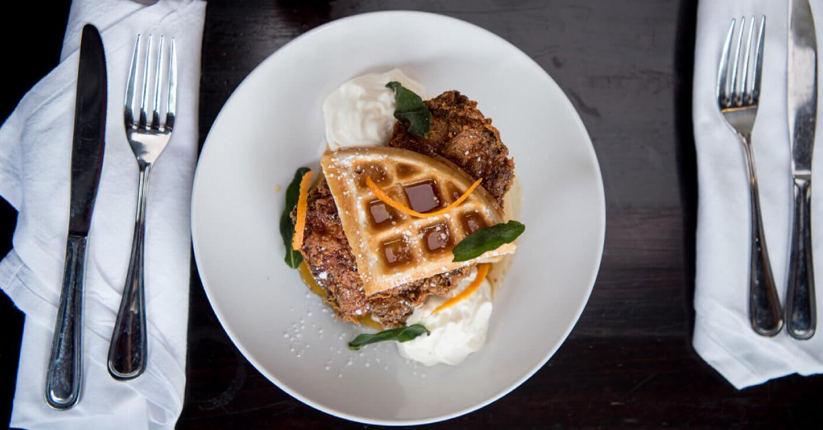 White plate with chicken and waffles on top and silverware to either side of plate