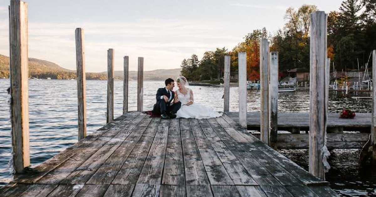 bride and groom sitting at the end of a dock on lake george