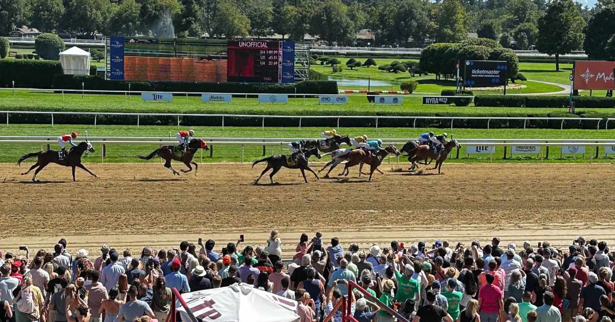 horses racing down dirt track with people watching