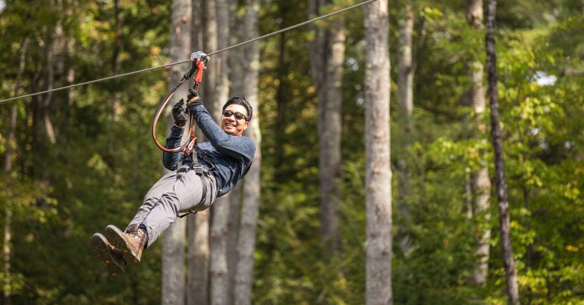 man wearing sunglasses ziplining in the woods