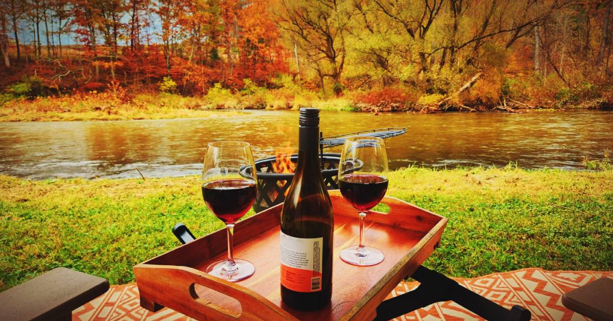 wine set out in front of campfire by river in fall