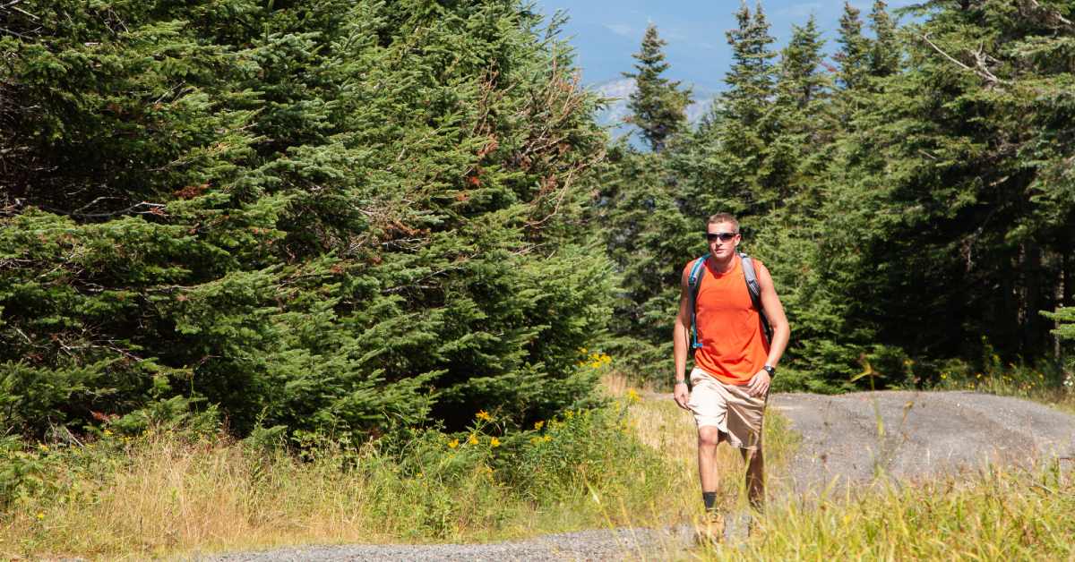 man in orange shirt and shorts hiking up trail
