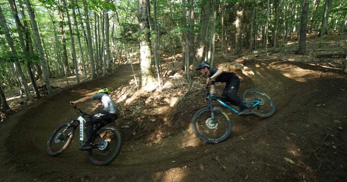 two people going around a corner on mountain bikes