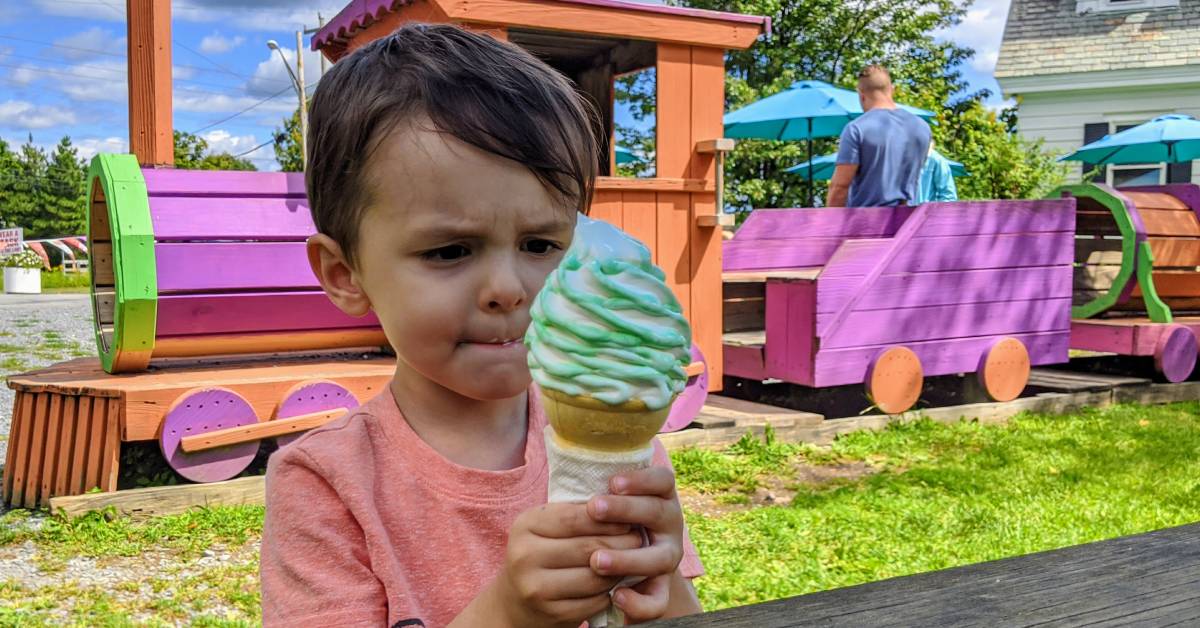 kid with ice cream cone at sprinkles with wooden train in background