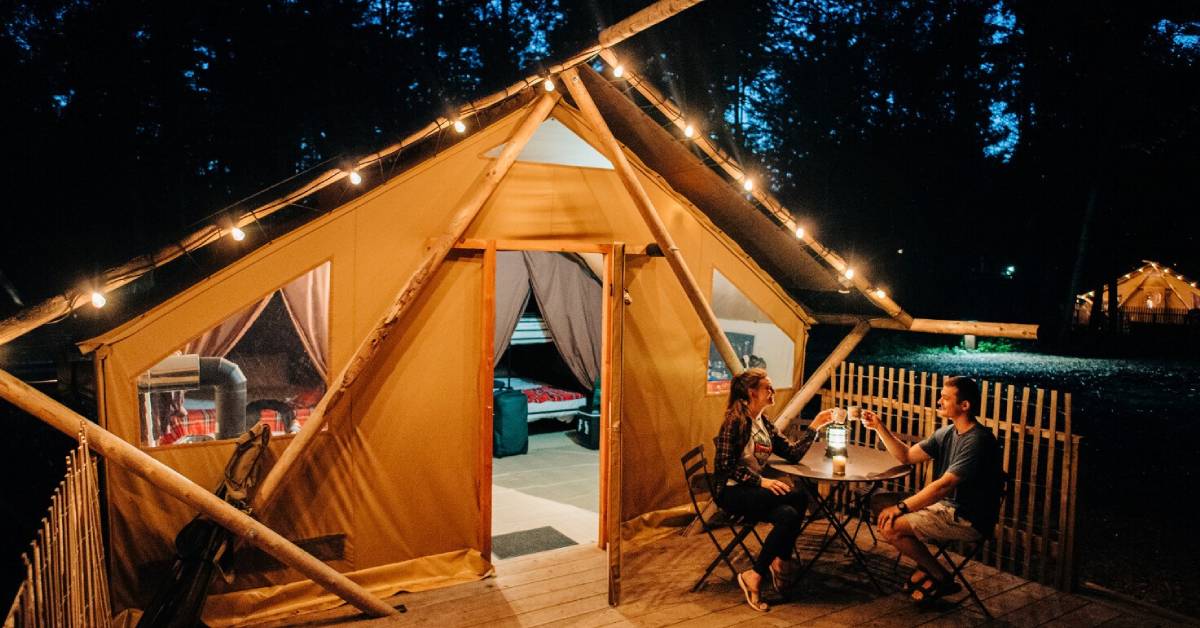 couple cheers coffee mugs outside glamping tent