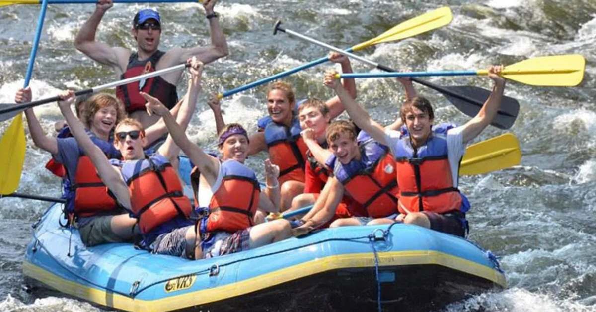large group of rafters holding paddles in the air