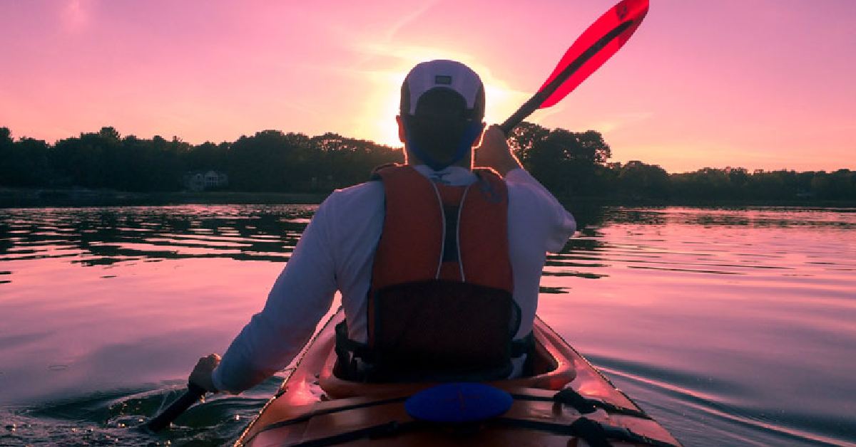 man kayaking on lake with sunset above
