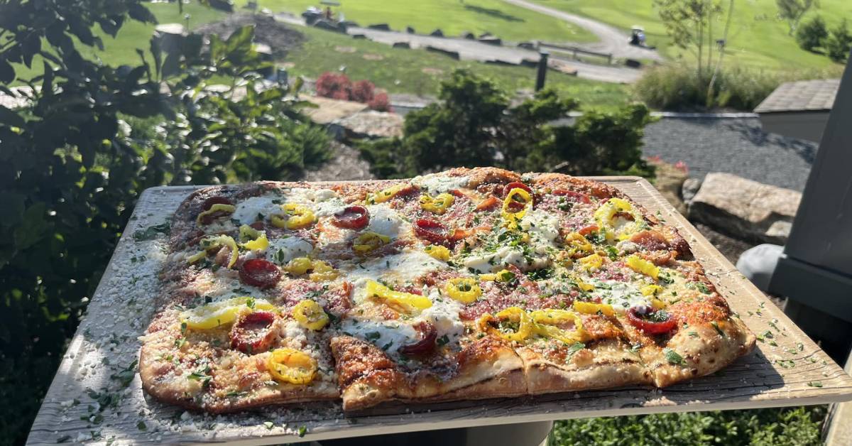 pizza held up against backdrop of ticonderoga golf course