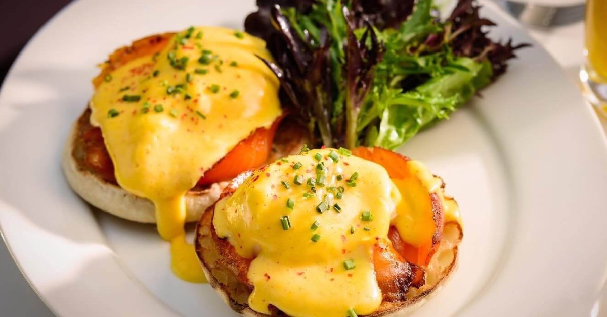 Dripping egg over an english muffin with greens in the background