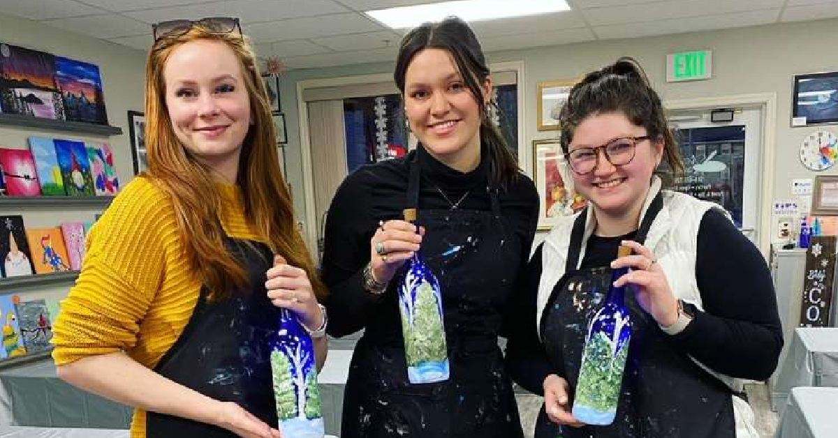 three women holding up painted bottles