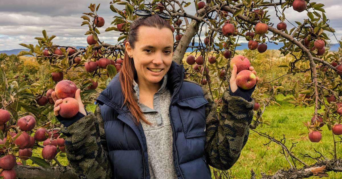 woman holds up apples at orchard