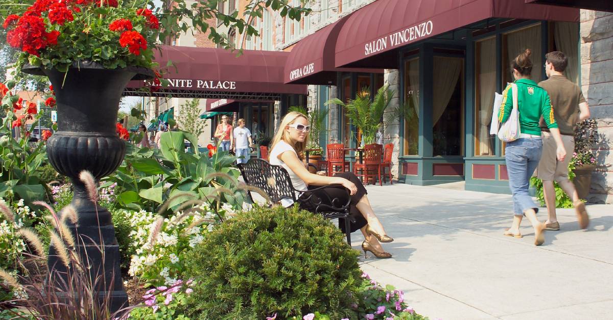 attractive woman sits on bench on broadway in saratoga with people walking by