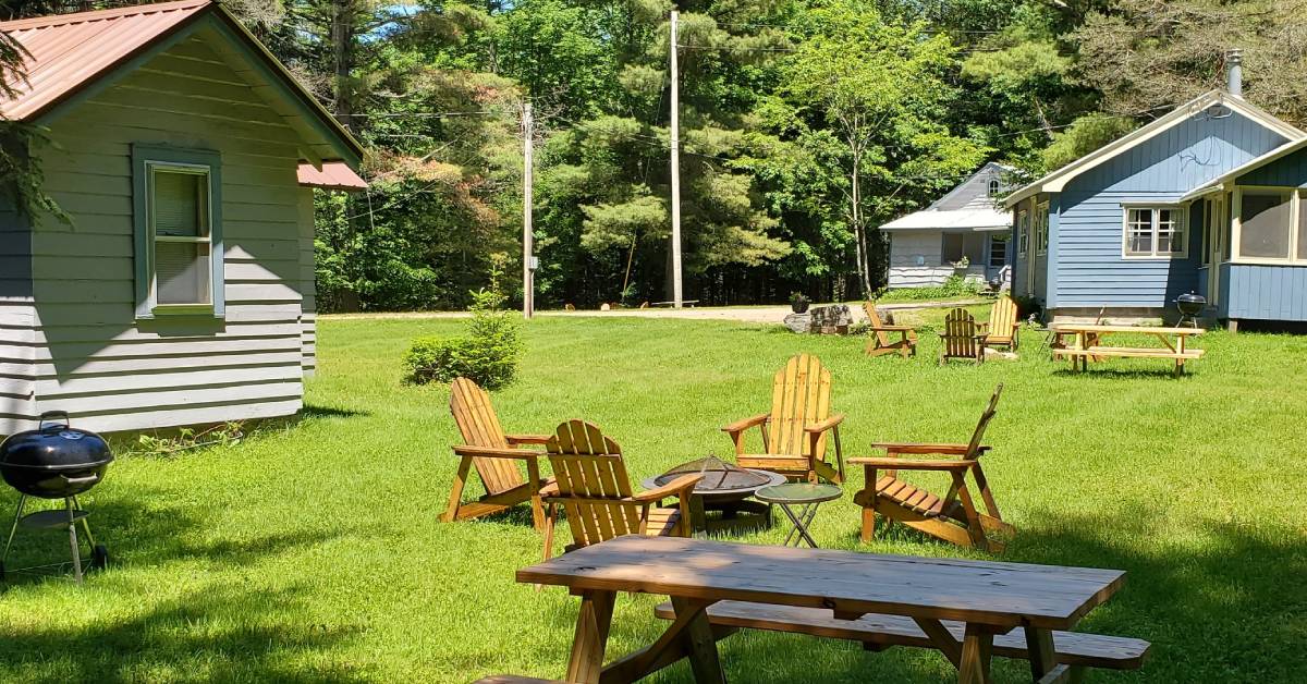 cabins and adirondack chairs around a fire pit, picnic tables, grill