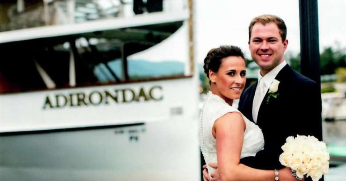 bride and groom posing in front of the adirondac boat