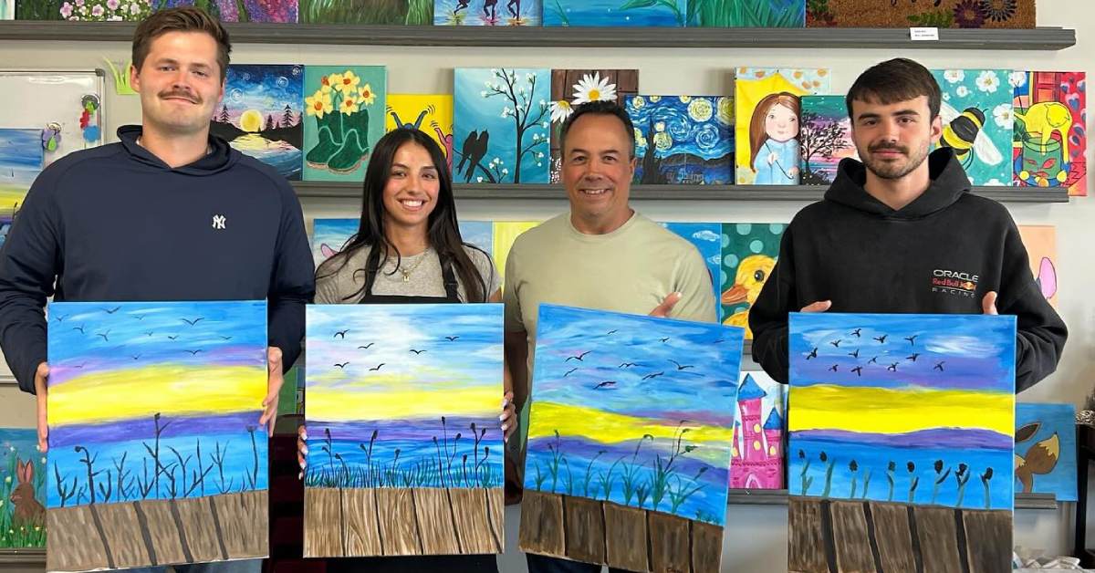 three men and a woman holding up paintings