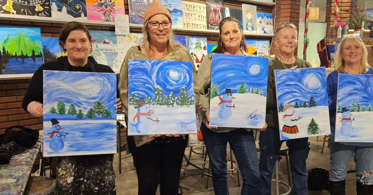 a group of women holding up winter paintings in a studio