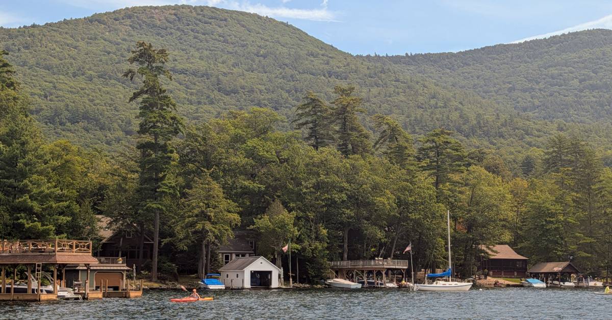lakefront houses, person kayaking, mountains in background