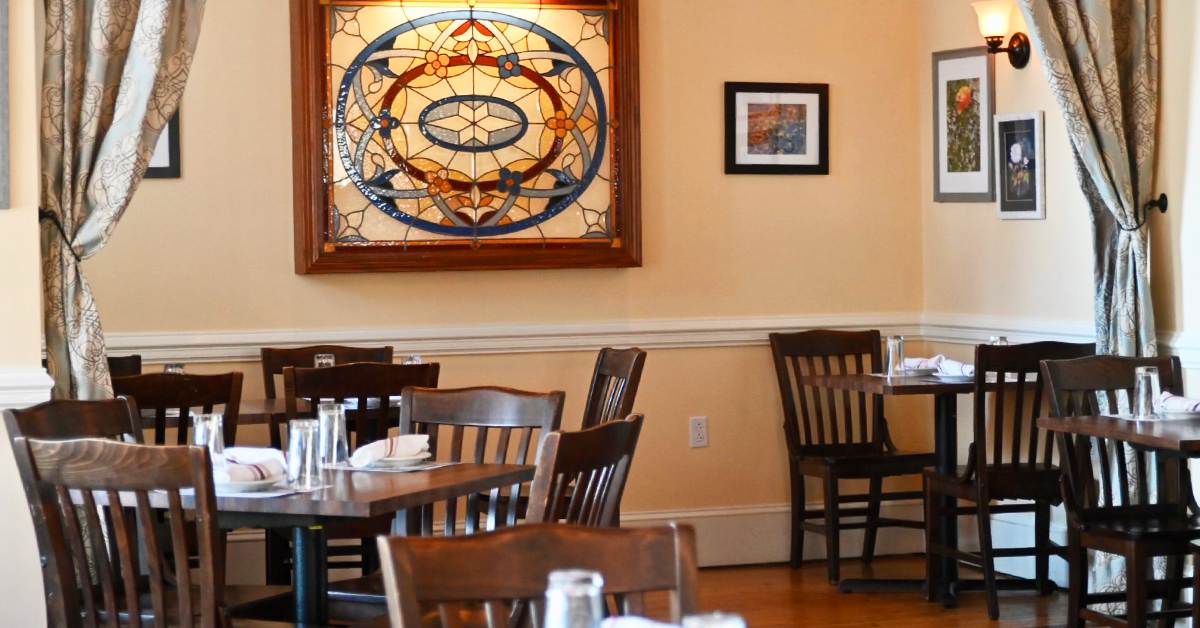 a restaurant dining room with tables, chairs, and ornate stained glass on wall