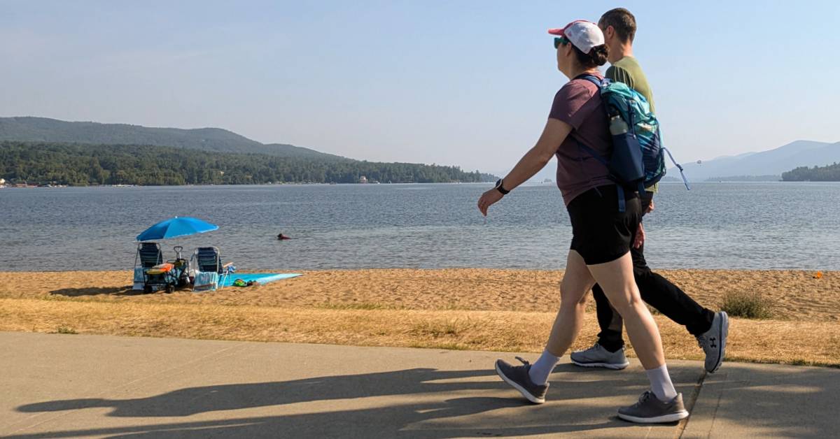 couple walks along beach road in lake george by the water