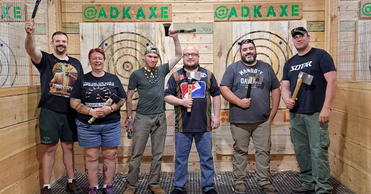 men and one woman pose at adirondack axe