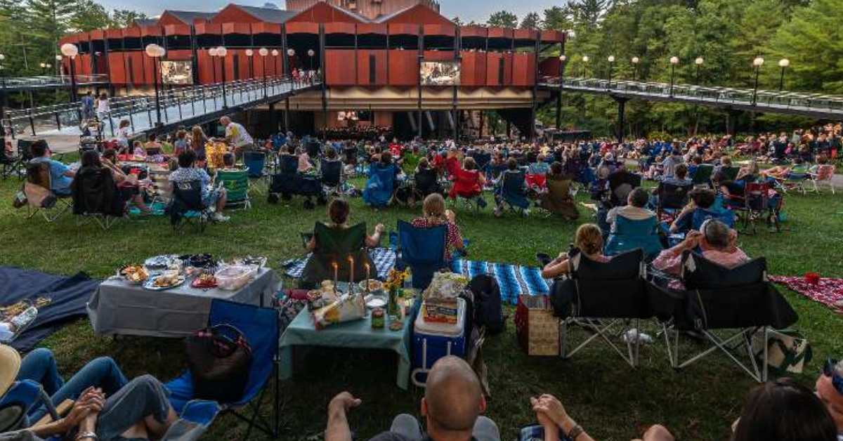 people sitting in chairs and on blankets outside an amphitheater 