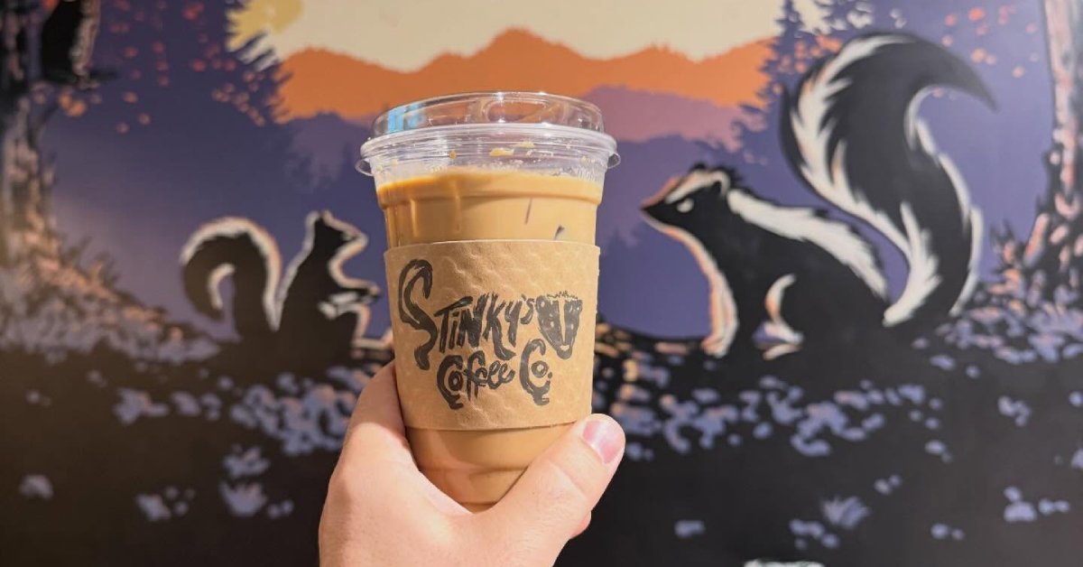 hand holding up a to-go cup of Stinky's Coffee with skunk artwork on the back wall