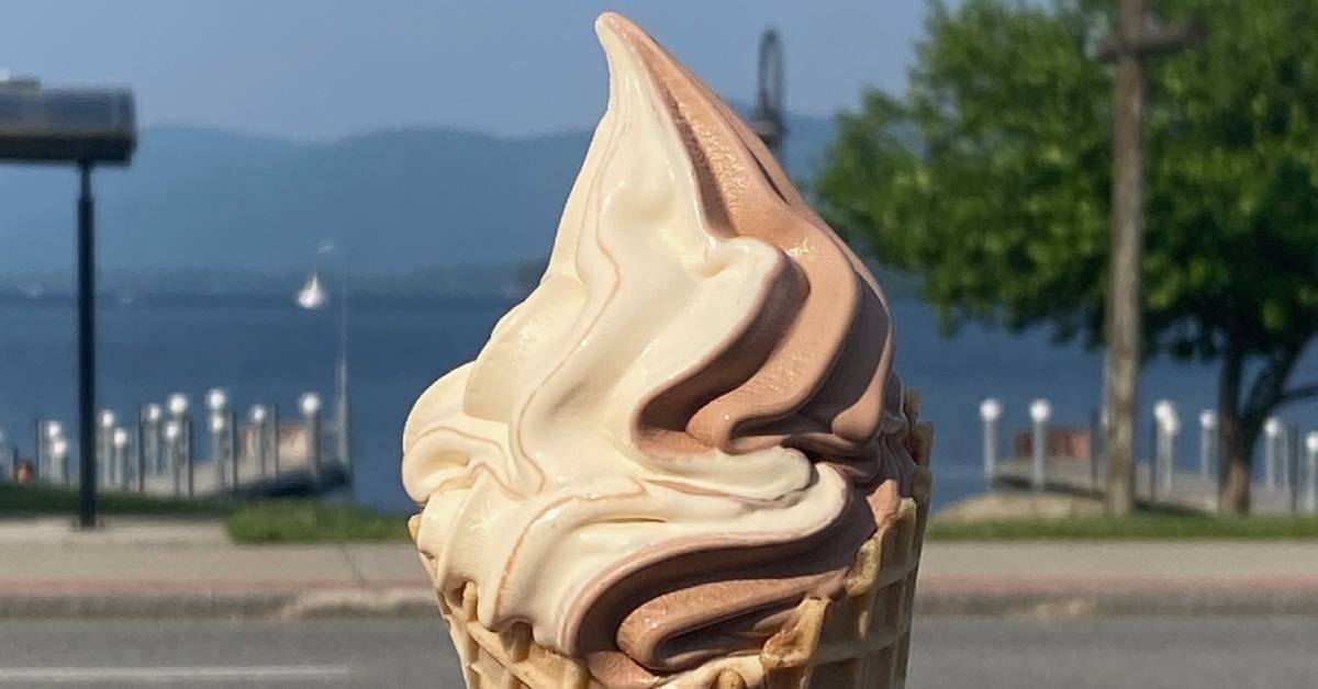 chocolate vanilla soft serve cone held up against lake george