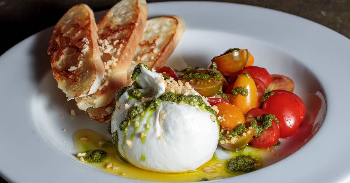 artfully plated bread, cheese, tomatoes with pesto sauce