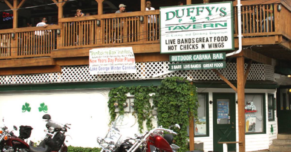 Exterior of Duffy’s Tavern in Lake George showing upper deck with people, bar signage, and bikes parked along the front