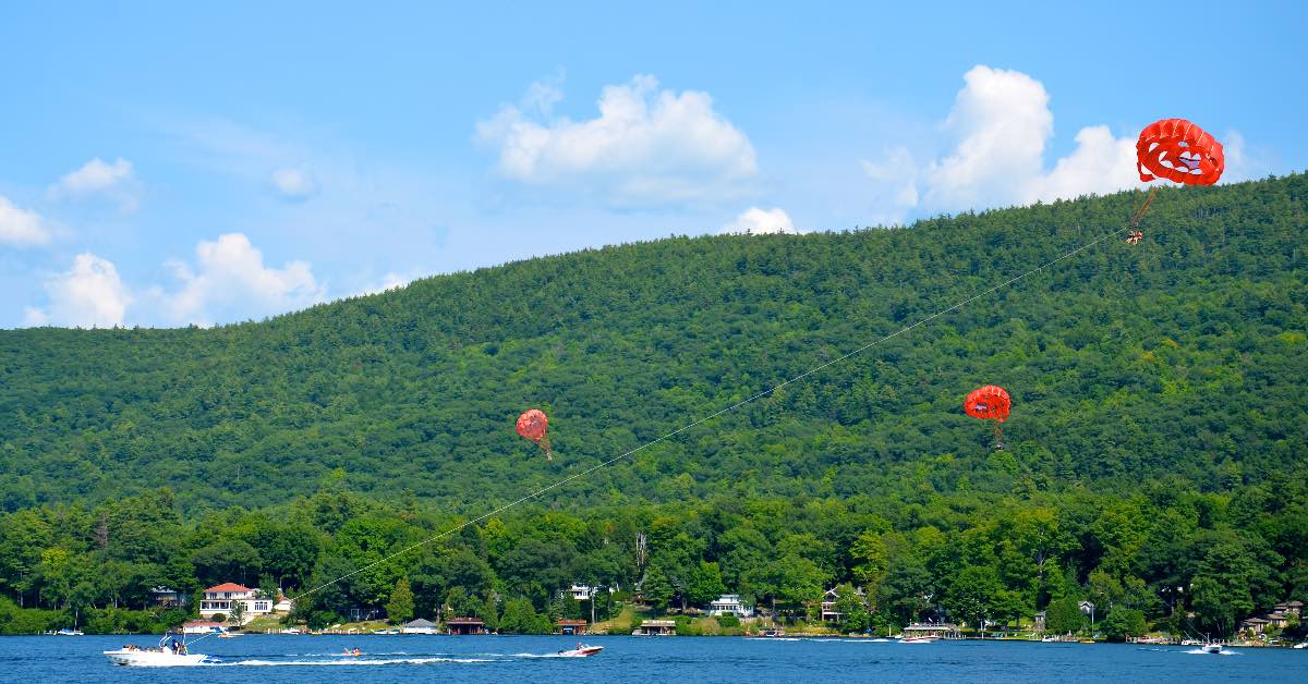 People parasailing above Lake George with colorful parachutes and boats pulling riders across the lake