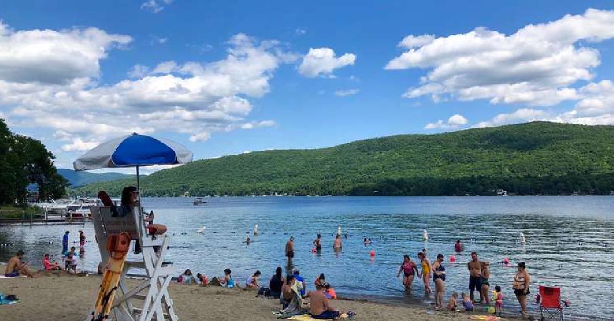 Busy day at Shepard Park in Lake George with swimmers in the water, people on the beach, and a lifeguard stand overlooking the shoreline