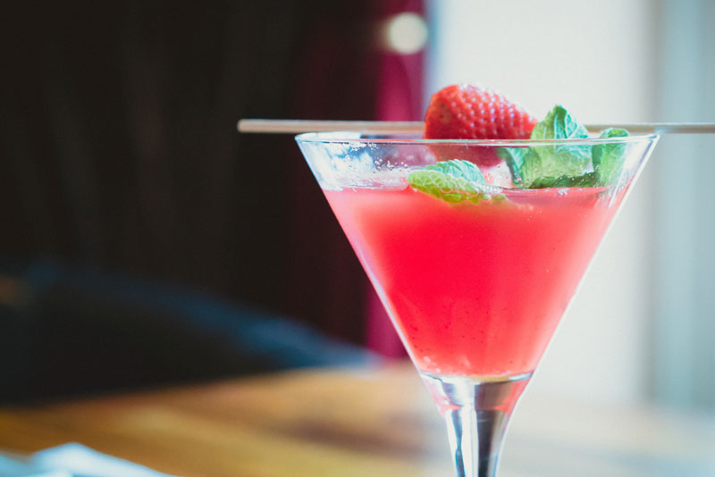 a red cocktail in a martini glass with a strawberry