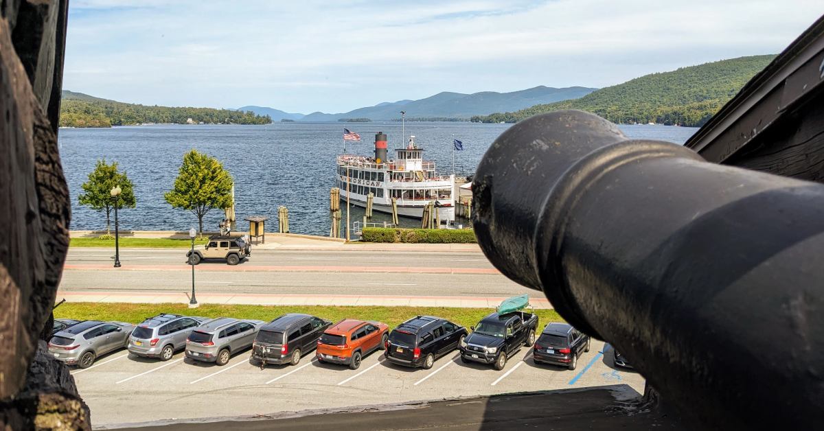 Fort William Henry Museum cannon overlooking Lake George with docked steamboat and Adirondack Mountains