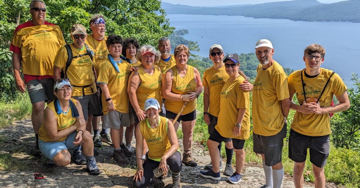 hikers in matching tee-shirts pose together with lake george in background