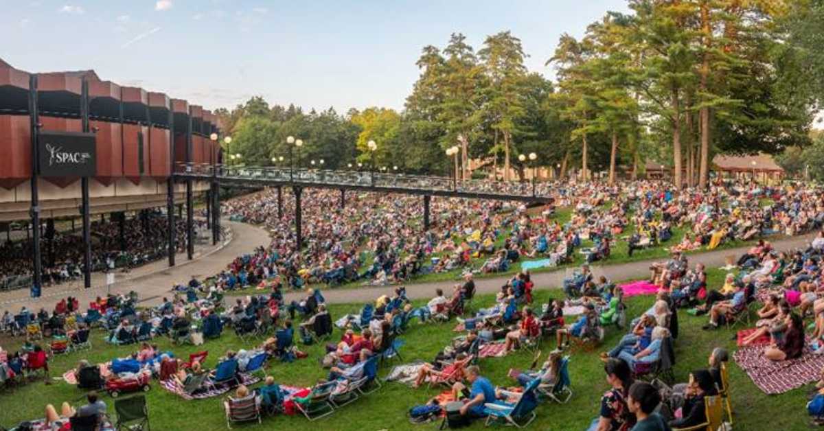people in chairs on a lawn outside an amphitheater