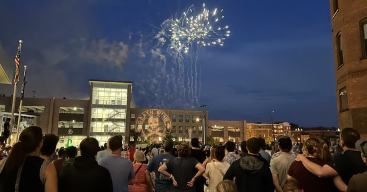 people in downtown city watching fireworks over building