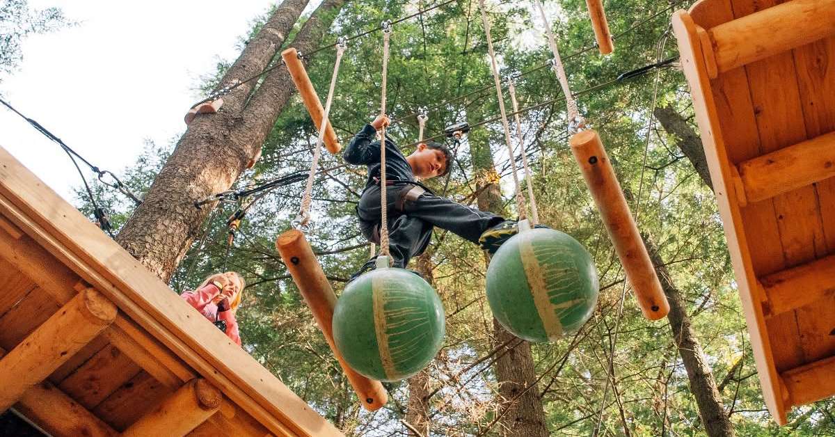 a teenager walking across a treetop adventure obstacle