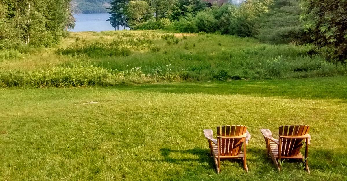 two adirondack chairs in field, water in the back