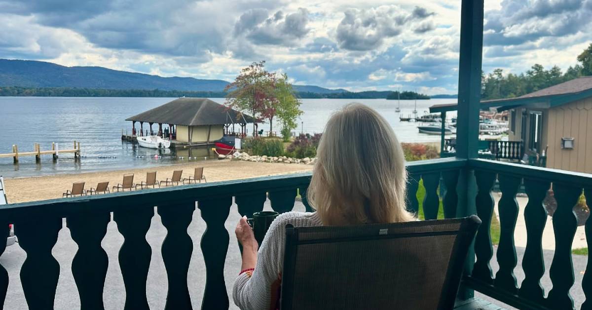 woman on balcony with coffee looks out at lake george