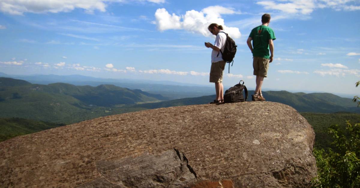 two men on summit, one looking at phone