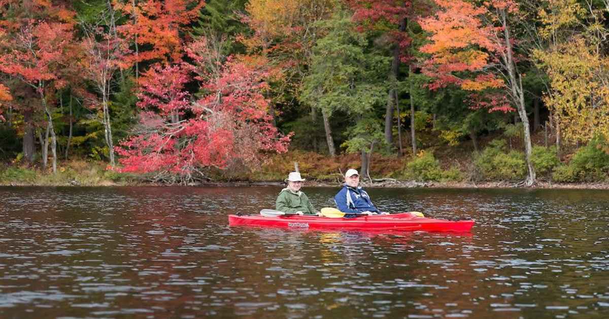 two men in a red kayak with fall colors on the trees