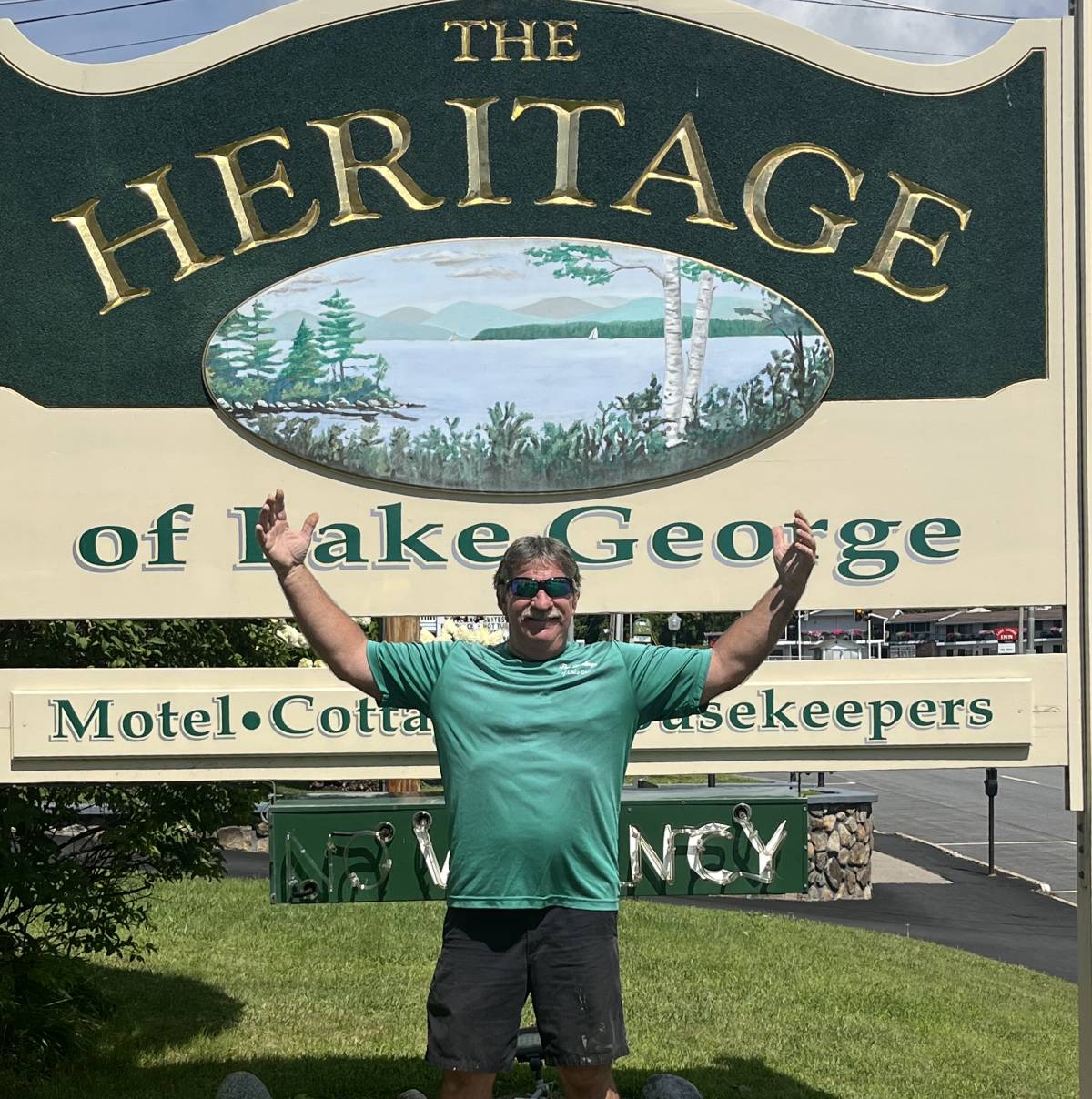 man stands in front of heritage of lake george sign