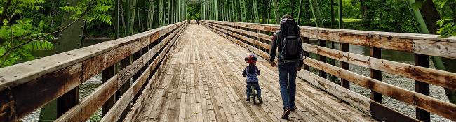 man with hiking backpack and kid on bike go over a bridge