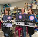women hold up paintings from a paint and sip of bears under a full moon