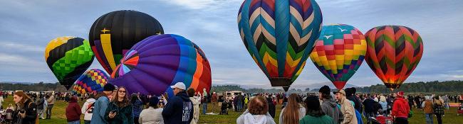 people at balloon festival looking at brightly colored hot air balloons about to lift up