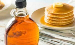maple syrup next to stacked pancakes with butter