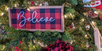 closeup of christmas tree with buffalo plaid sign saying believe