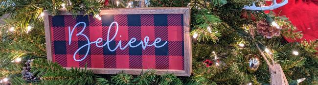 closeup of christmas tree with buffalo plaid sign saying believe