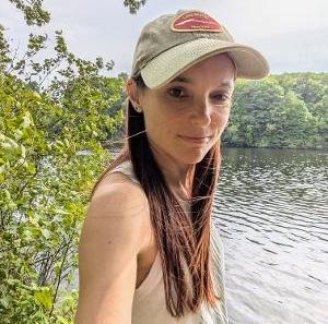woman in hat poses in front water